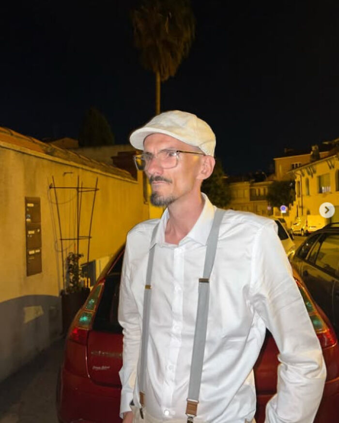 Man in white shirt and cap stands near parked cars at night, highlighting latest streamer tragedy and toxic online challenges.