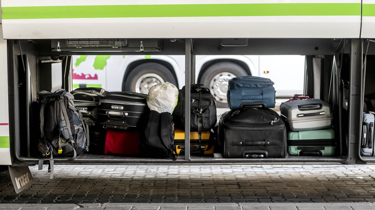 Bus luggage compartment open showing multiple suitcases and bags tightly packed inside storage area.