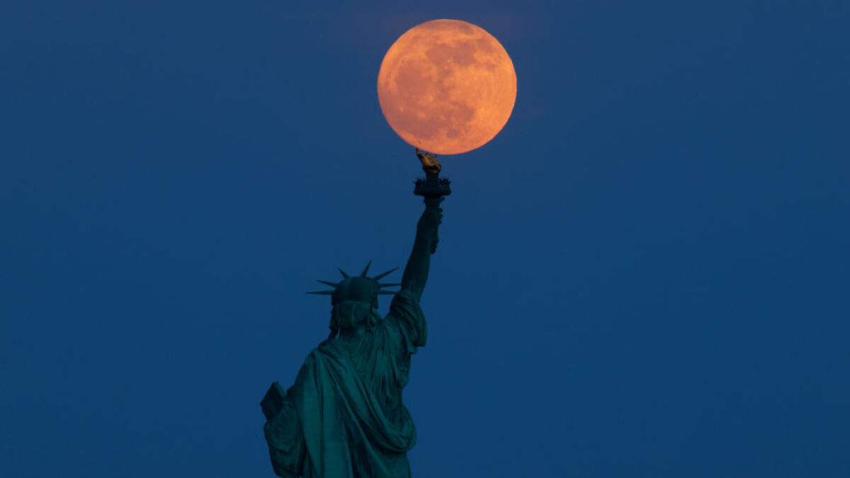 Statue of Liberty holding torch aligned with full moon in dark sky illustrating nuclear reactor on the Moon concept.