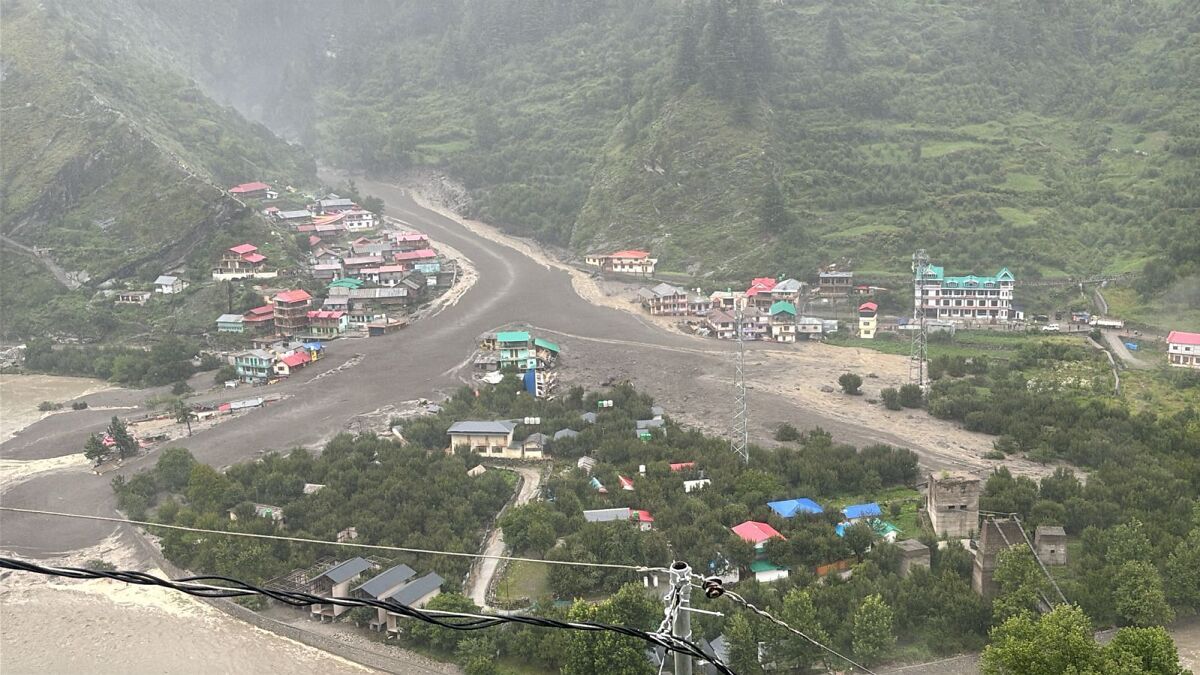 Mountain town with severe flash floods sweeping through riverbanks and surrounding buildings in a green valley area.