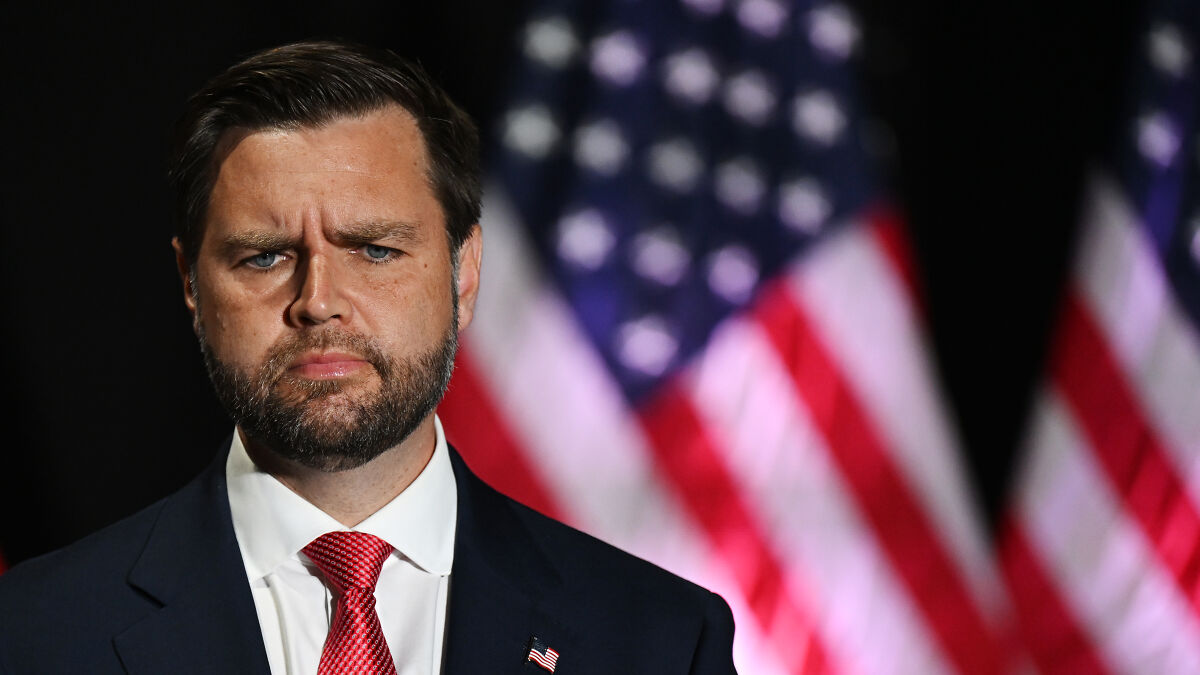 J.D. Vance serious expression indoors with blurred American flags in background, related to river water level issue.