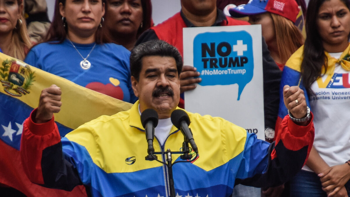 Venezuelau2019s President Nicolu00e1s Maduro speaking at a rally with protesters and Venezuelan flags in the background.