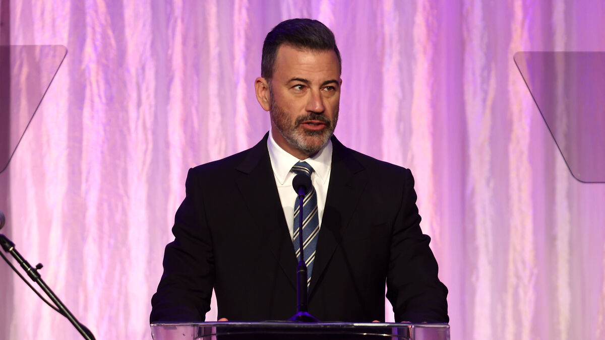 Jimmy Kimmel speaking at a podium in a suit and tie, discussing new citizenship amid celebrities leaving the U.S.