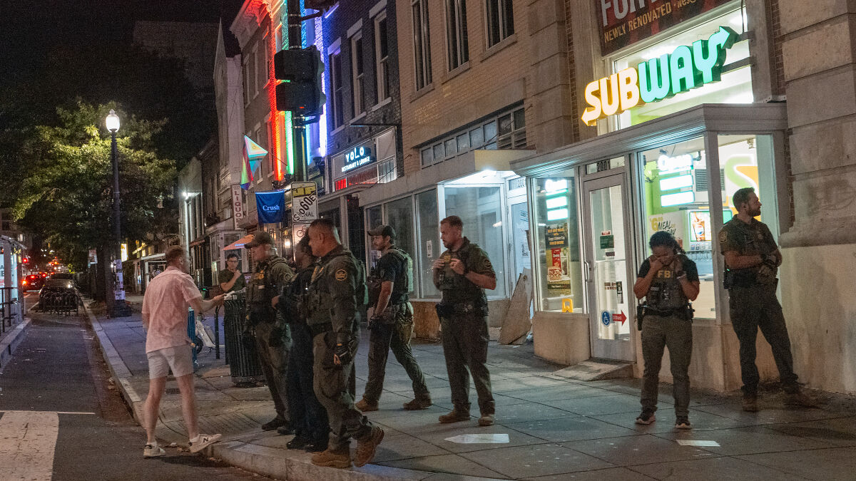 Man in pink shirt confronts law enforcement officers outside Subway restaurant on a city street at night.