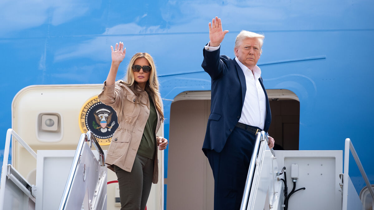 Melania Trump and Donald Trump waving on airplane stairs with presidential seal in daylight