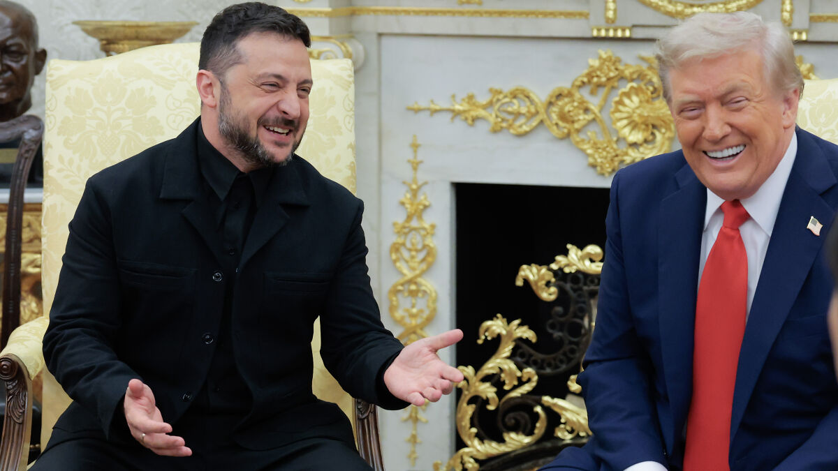 Volodymyr Zelenskyy in a black suit sitting and smiling during a White House meeting with Donald Trump.