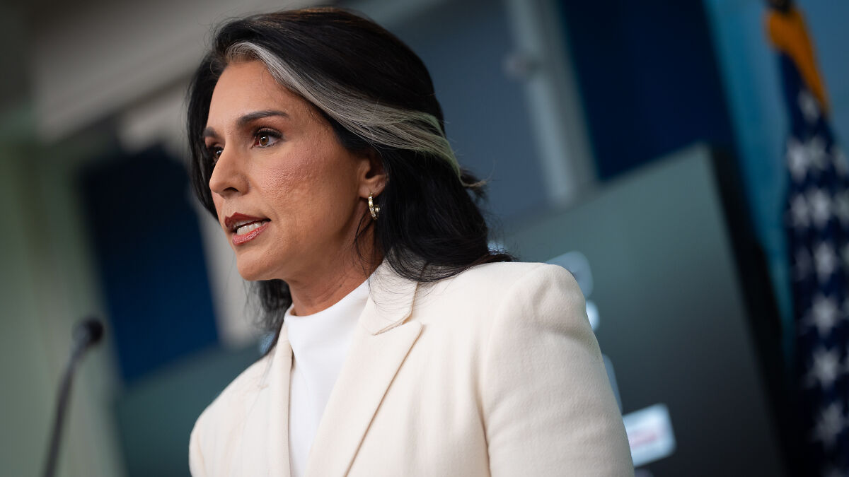 Tulsi Gabbard in a white jacket speaking at a podium about revoking clearances for alleged intelligence subversion.