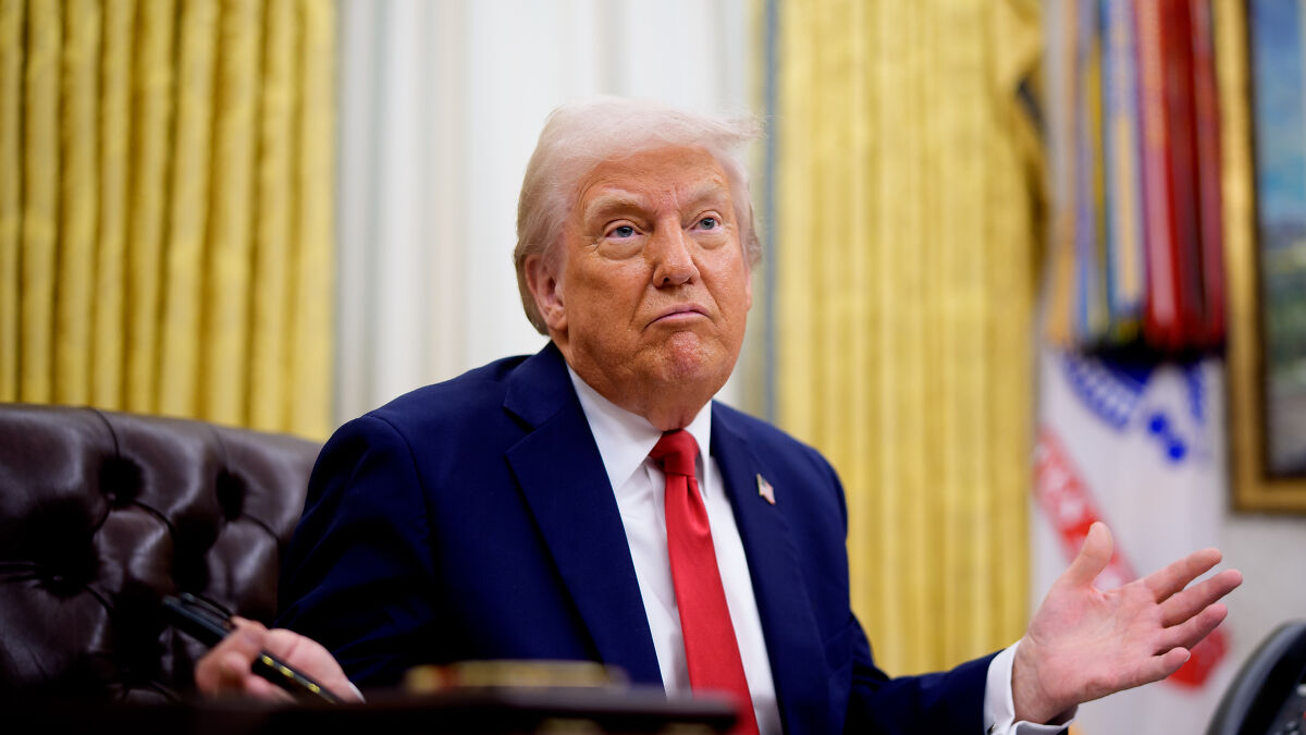 Donald Trump in the Oval Office, wearing a blue suit and red tie, reacting to news about Chinese students admission.