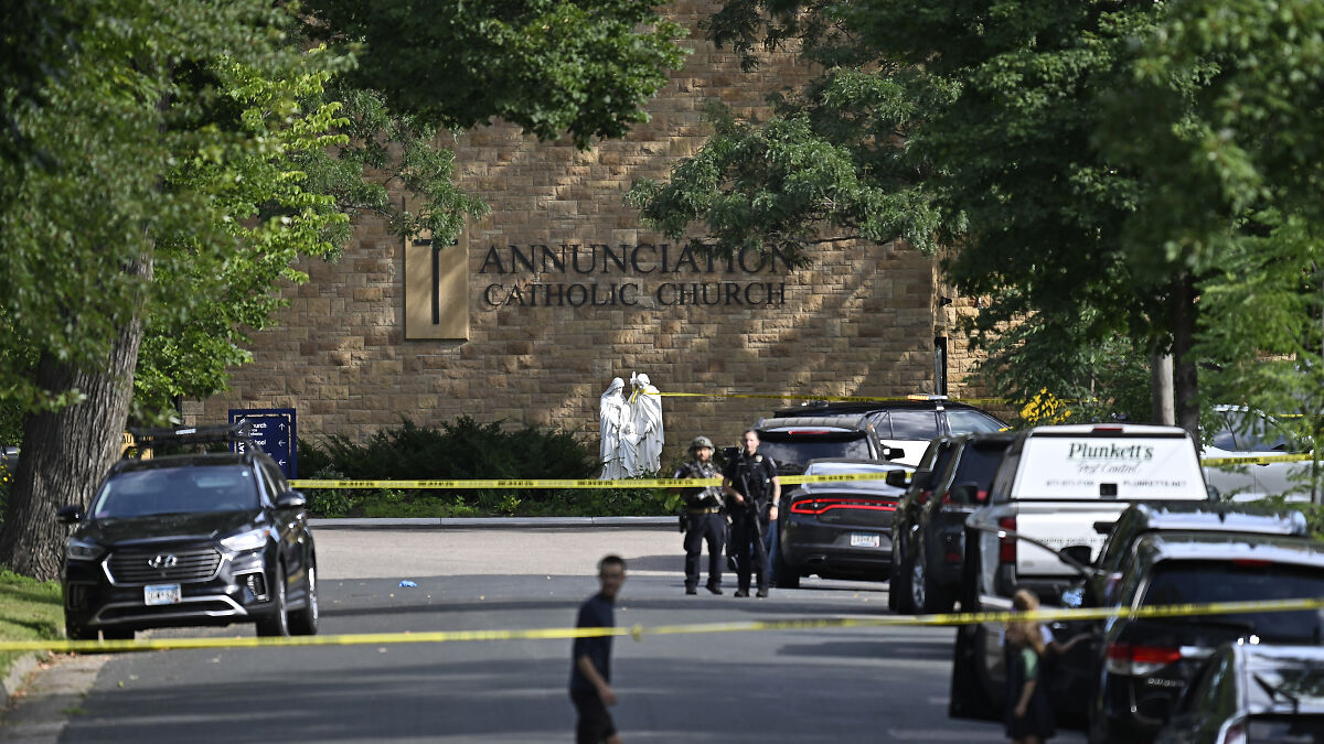 Police officers and yellow tape cordon off area near Catholic church during Minneapolis school tragedy investigation.
