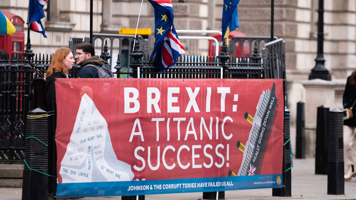 Protest banner in post-Brexit Britain with British and EU flags, highlighting IMF bailout concerns and political criticisms.