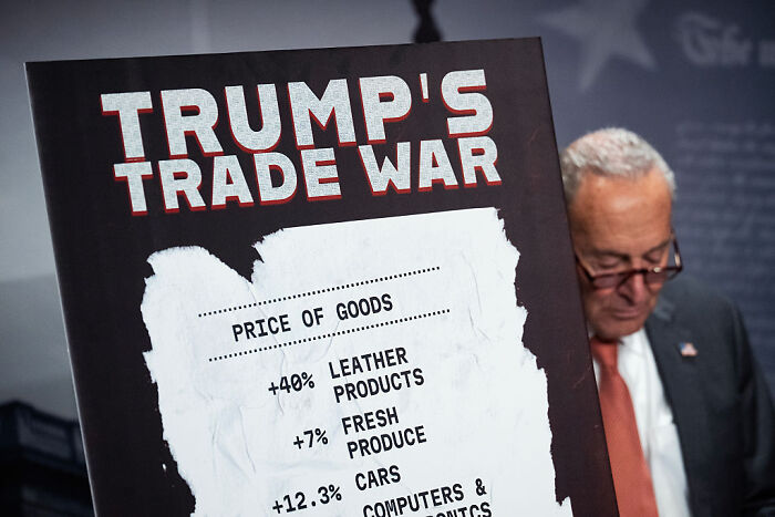 Man holding a sign showing price increases during Trump's trade war as Americans struggle to afford essentials.
