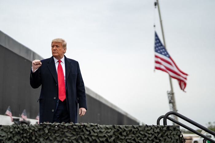 Former President Trump standing near an American flag, related to Bad Bunny triggering MAGA outrage after Super Bowl halftime show.