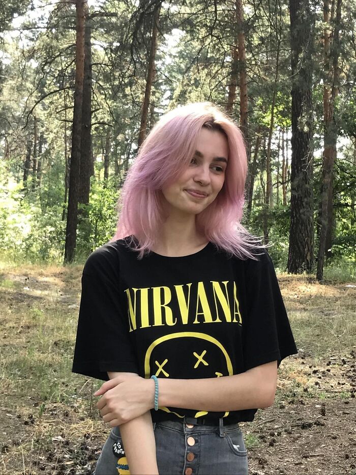 Young woman with pink hair wearing a Nirvana shirt standing in a forest, related to Ukrainian refugee stabbing incident. Young woman with pink hair wearing a Nirvana shirt standing in a forest, related to Ukrainian refugee stabbing incident.
