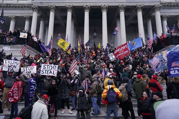 Crowd of protesters with flags and signs on courthouse steps highlighting America’s escalating political violence concerns.