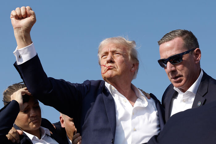 Former President raising fist with bleeding lip, surrounded by security, illustrating America's escalating political violence concerns.