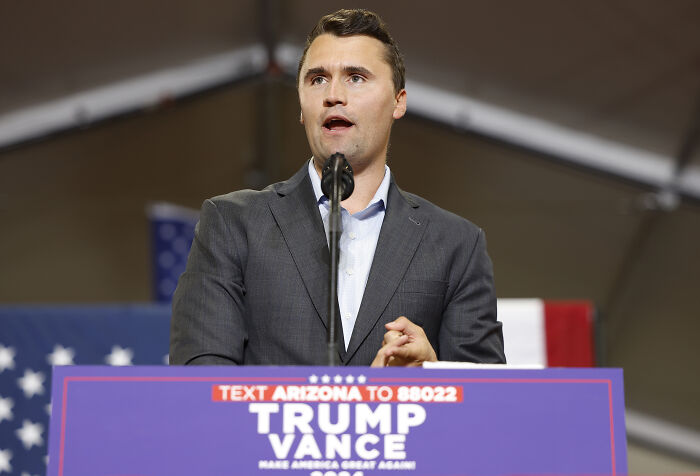 Man speaking at podium with Trump Vance sign, addressing issues related to Charlie Kirk shooting suspect Tyler Robinson.