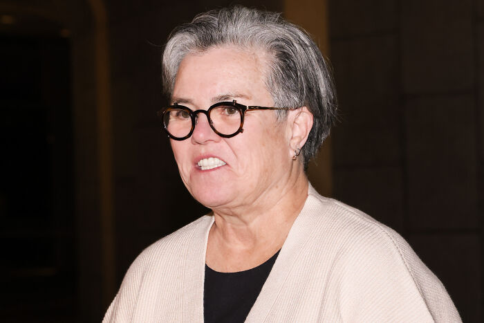 Rosie O’Donnell wearing glasses and a beige sweater, speaking publicly about MAGA and Minnesota school shooter remark.