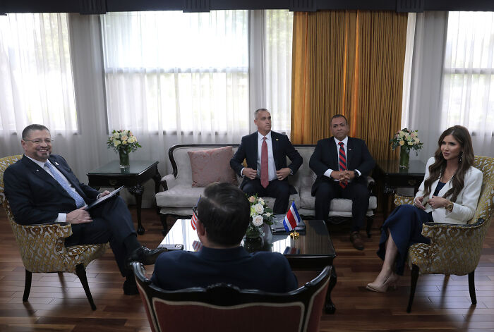 Group of five people in formal attire seated in a bright room discussing the Trump camp and Kristi ICE Barbie Noem affair claims.