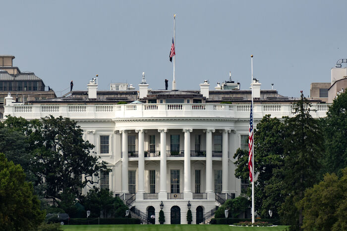 The White House with American flags at half-staff symbolizing concerns over America’s escalating political violence.