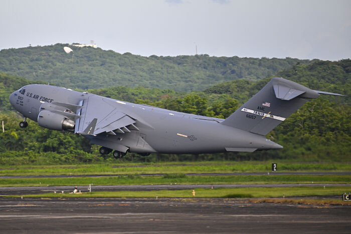 US Air Force cargo plane taking off with green hills in the background related to JD Vance’s Venezuelan boat joke news.