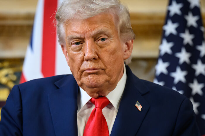Former president wearing a suit and red tie in front of American flags during a formal event discussing JD Vance’s Venezuelan boat joke controversy