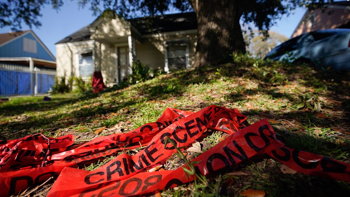 Red crime scene tape lying on grass near a Houston home, related to boy fatally shot during doorbell prank.