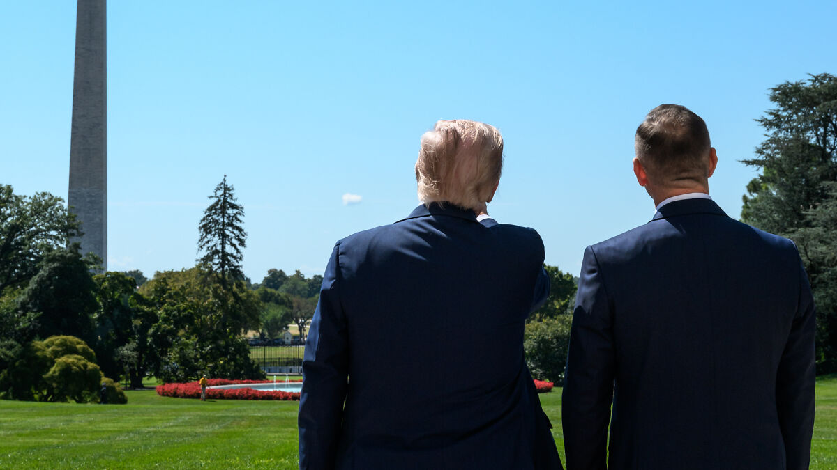 Two men in suits standing outdoors near the Washington Monument during a loud jet flyover disrupting an Epstein victims rally