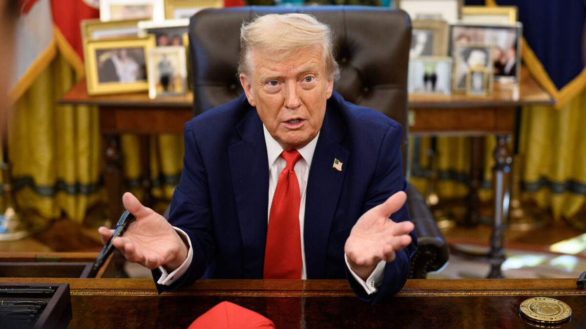 Former President Trump speaking at desk, wearing navy suit and red tie, addressing domestic violence controversy.