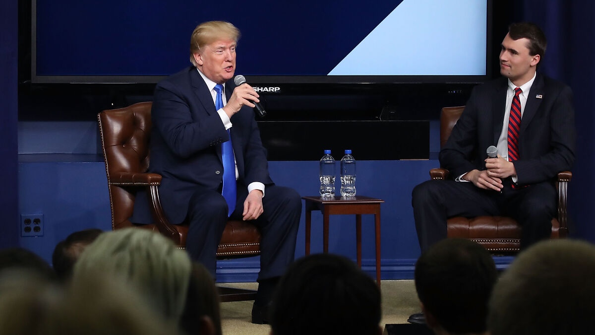 Politician speaking into microphone seated by another man in suit and tie discussing firearm fatalities in formal setting.