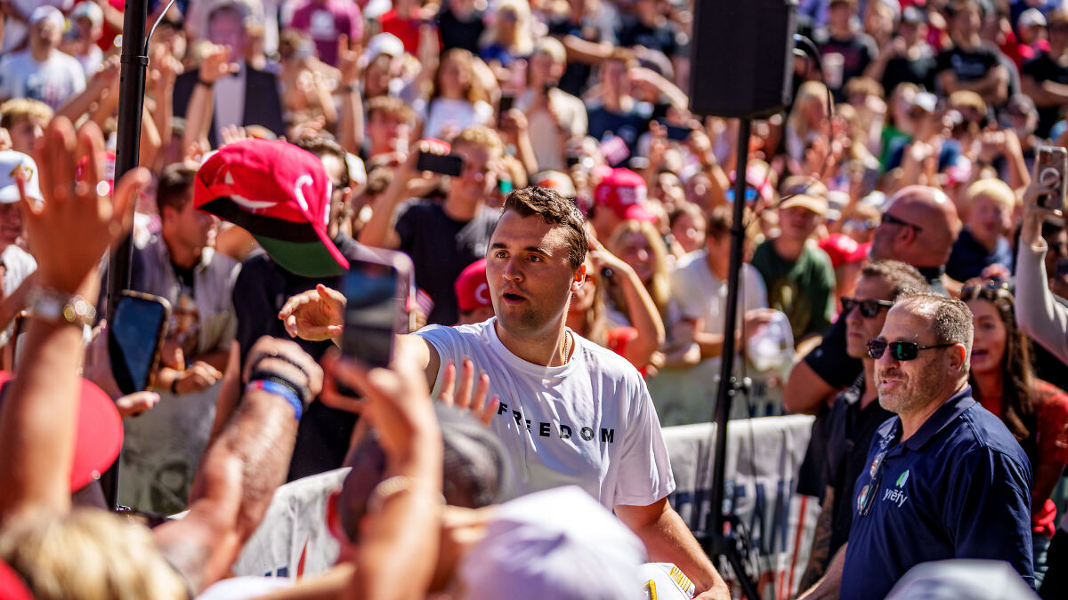 Charlie Kirk engaging with a crowd at an outdoor event, surrounded by supporters and security personnel.
