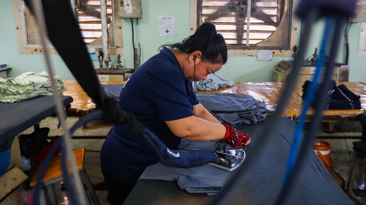 Woman ironing fabric in a factory, illustrating the impact of Trumps trade war costing billions on manufacturing jobs.