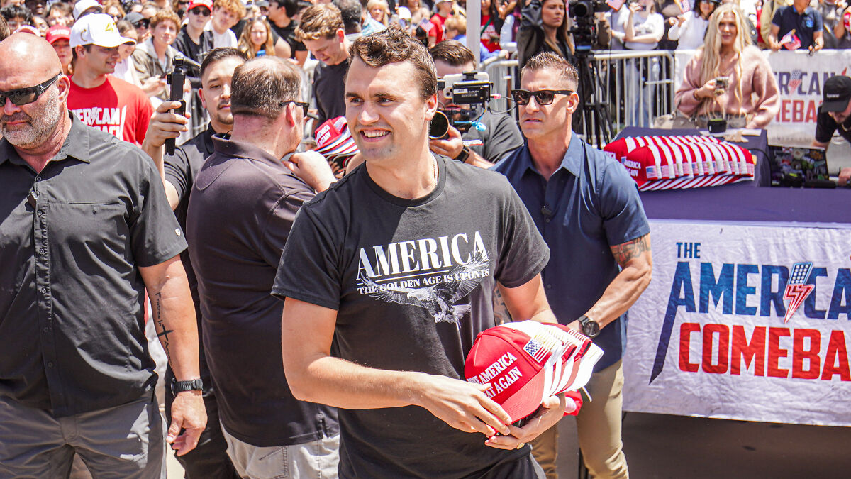 Man holding red Make America Great Again hats at crowded event with political violence concerns in America.
