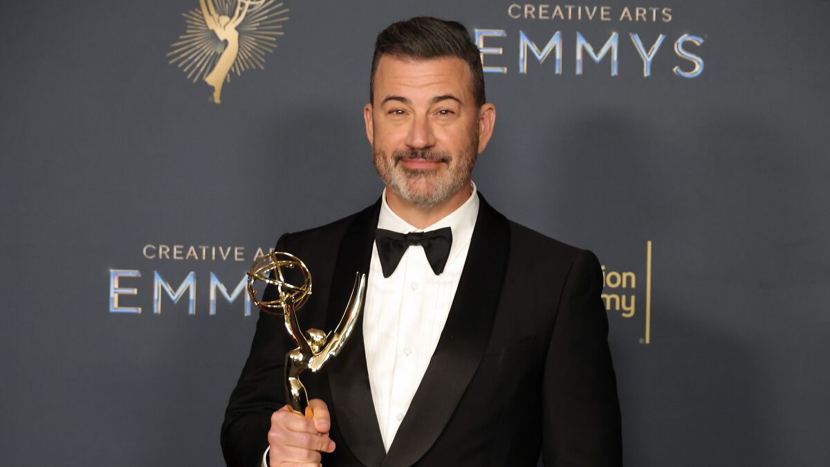 Jimmy Kimmel holding an Emmy award, dressed in a tuxedo at the Creative Arts Emmys event.