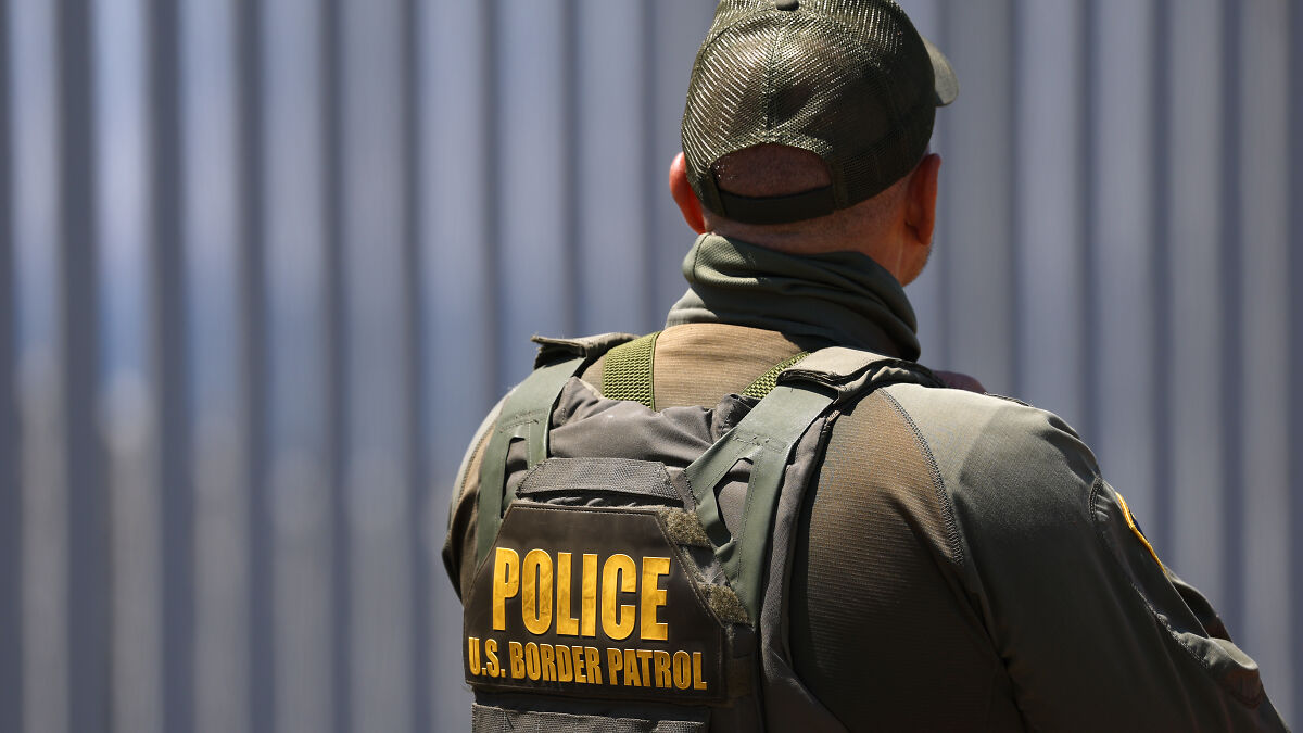 U.S. Border Patrol agent wearing tactical gear standing near a metal barrier, linked to ICE detaining autistic girl case.