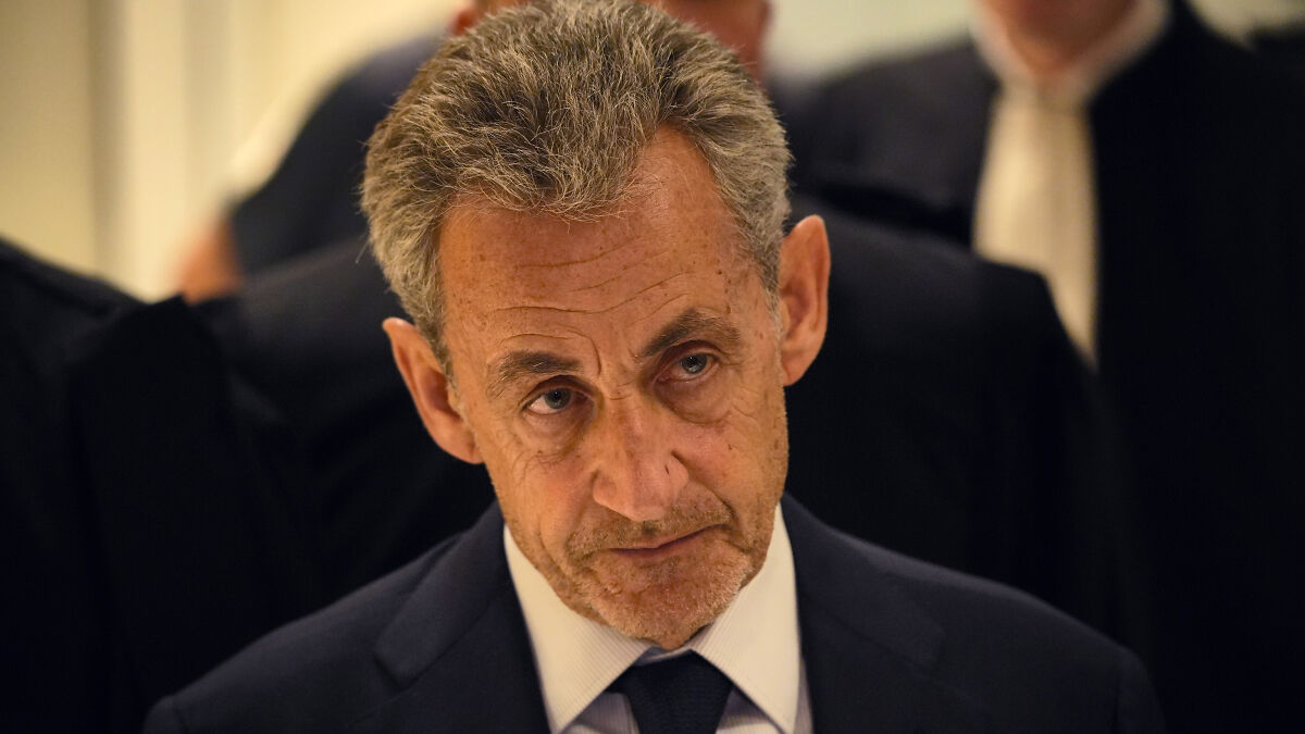 Former French President Nicolas Sarkozy in a serious expression, wearing a dark suit at a formal event.