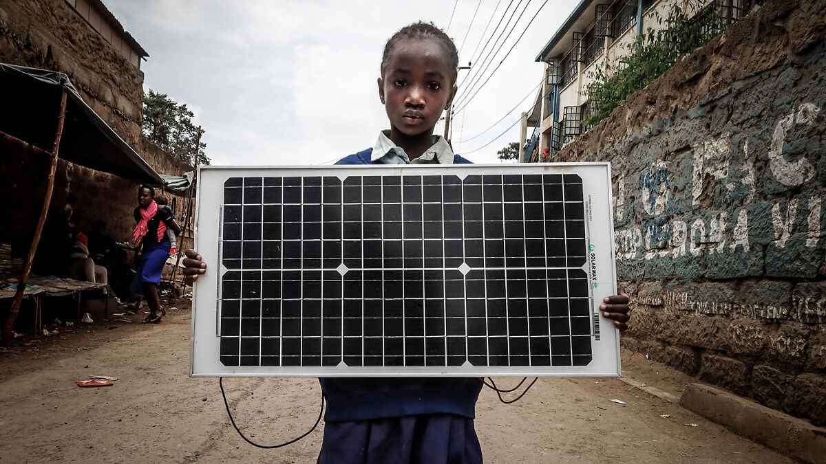 Young girl holding a solar panel in an African urban area illustrating the solar power plant boom in Africa.
