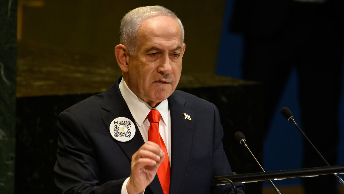 Benjamin Netanyahu speaking at UN General Assembly podium, wearing a dark suit and red tie.