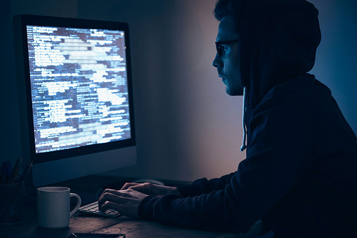 Person wearing a hoodie working on a desktop computer with code on screen, related to free speech social media laws UK.