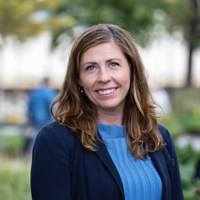 Sweden’s new health minister outdoors, smiling with shoulder-length hair, wearing a blue top and dark blazer in natural setting