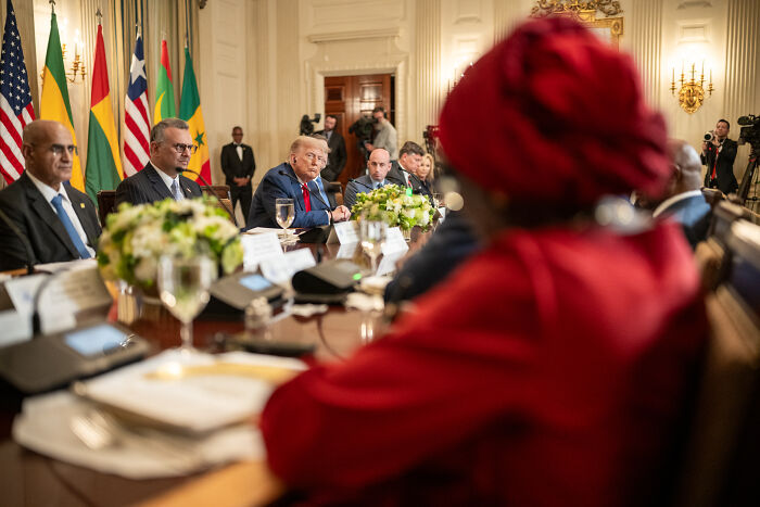 Donald Trump at a formal meeting discussing trade policies with international delegates amid trade war costing billions concerns.