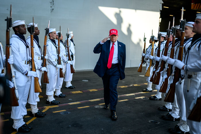 Former President Trump in a red USA hat salutes naval officers amid rising tensions between U.S. and Venezuela. Former President Trump in a red USA hat salutes naval officers amid rising tensions between U.S. and Venezuela.