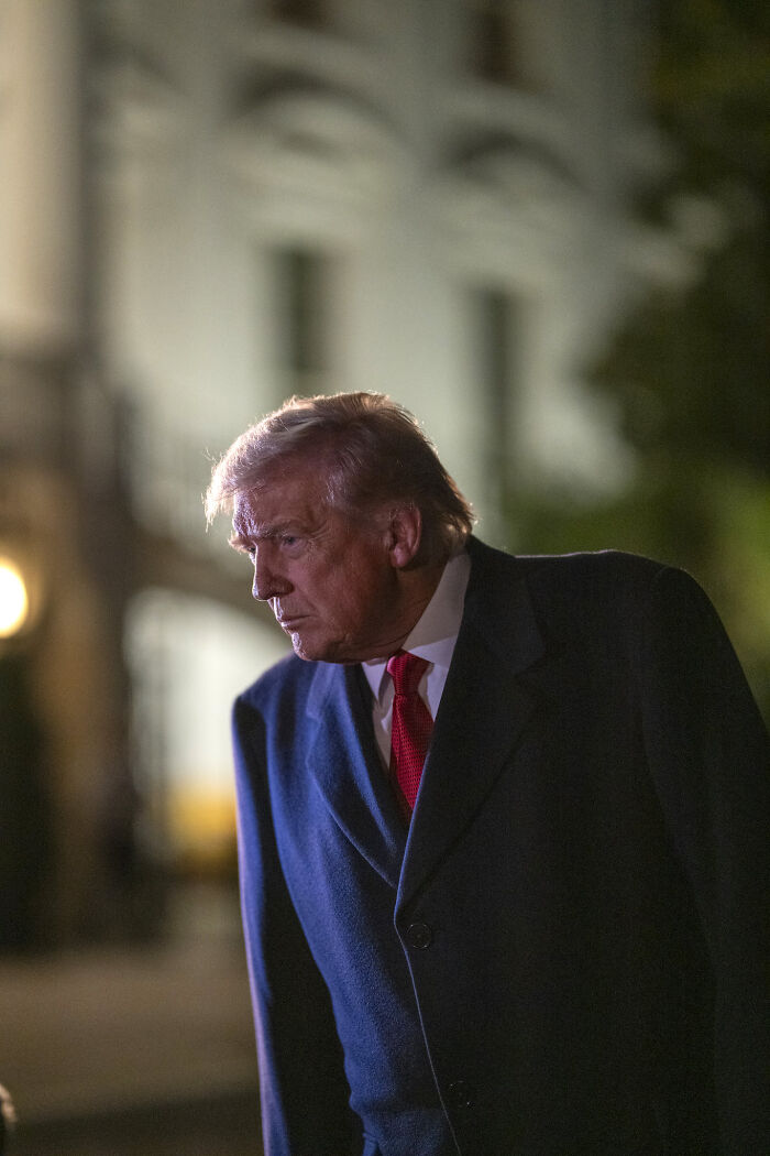 Donald Trump outdoors at night wearing a dark coat and red tie in a candid moment with blurred background. Donald Trump outdoors at night wearing a dark coat and red tie in a candid moment with blurred background.