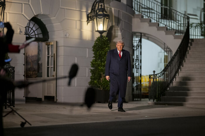 Former President Trump walking outside White House at night during media coverage on visa-related issue. Former President Trump walking outside White House at night during media coverage on visa-related issue.