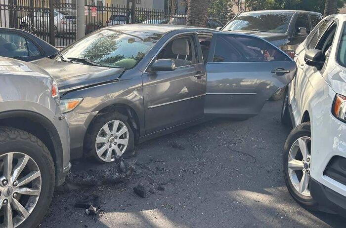 Damaged gray car with open door between two vehicles, related to LA TikToker filming ICE raids during immigration operation.