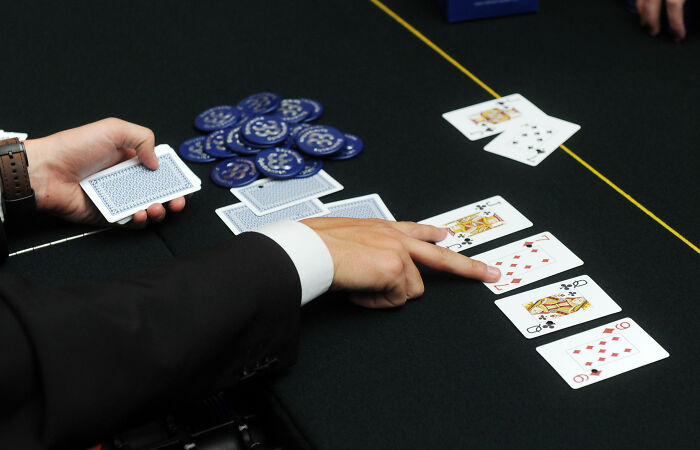 Man in suit pointing at playing cards on a table with poker chips, related to NBA gambling and insider bets. Man in suit pointing at playing cards on a table with poker chips, related to NBA gambling and insider bets.