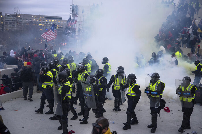 Police in riot gear standing amid smoke during January 6 event with crowd in background, highlighting prosecutors and DOJ leave. Police in riot gear standing amid smoke during January 6 event with crowd in background, highlighting prosecutors and DOJ leave.