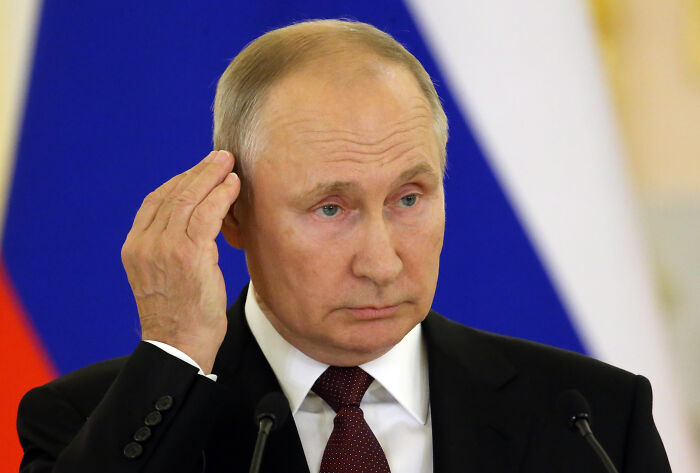 Vladimir Putin speaking at a podium with Russian flag colors in the background, relating to Putin’s war in Ukraine.