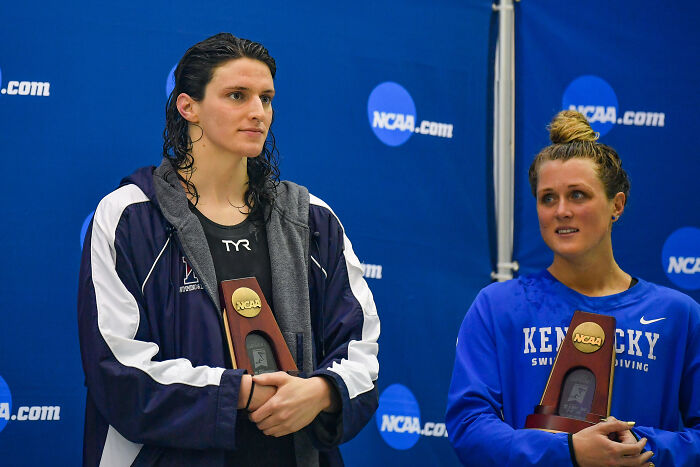 Two female swimmers holding NCAA trophies at an award ceremony, related to AOC’s viral tweet clapping back. Two female swimmers holding NCAA trophies at an award ceremony, related to AOC’s viral tweet clapping back.