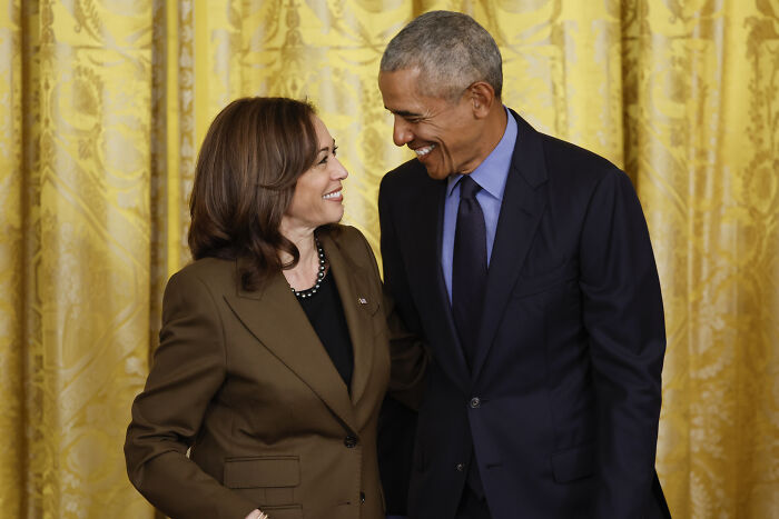 Barack Obama and Kamala Harris smiling at each other in a formal setting with gold curtains in the background Barack Obama and Kamala Harris smiling at each other in a formal setting with gold curtains in the background