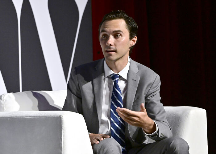 Man in gray suit and striped tie speaking while seated on a white chair at a panel discussion about David Hogg PAC consultants.